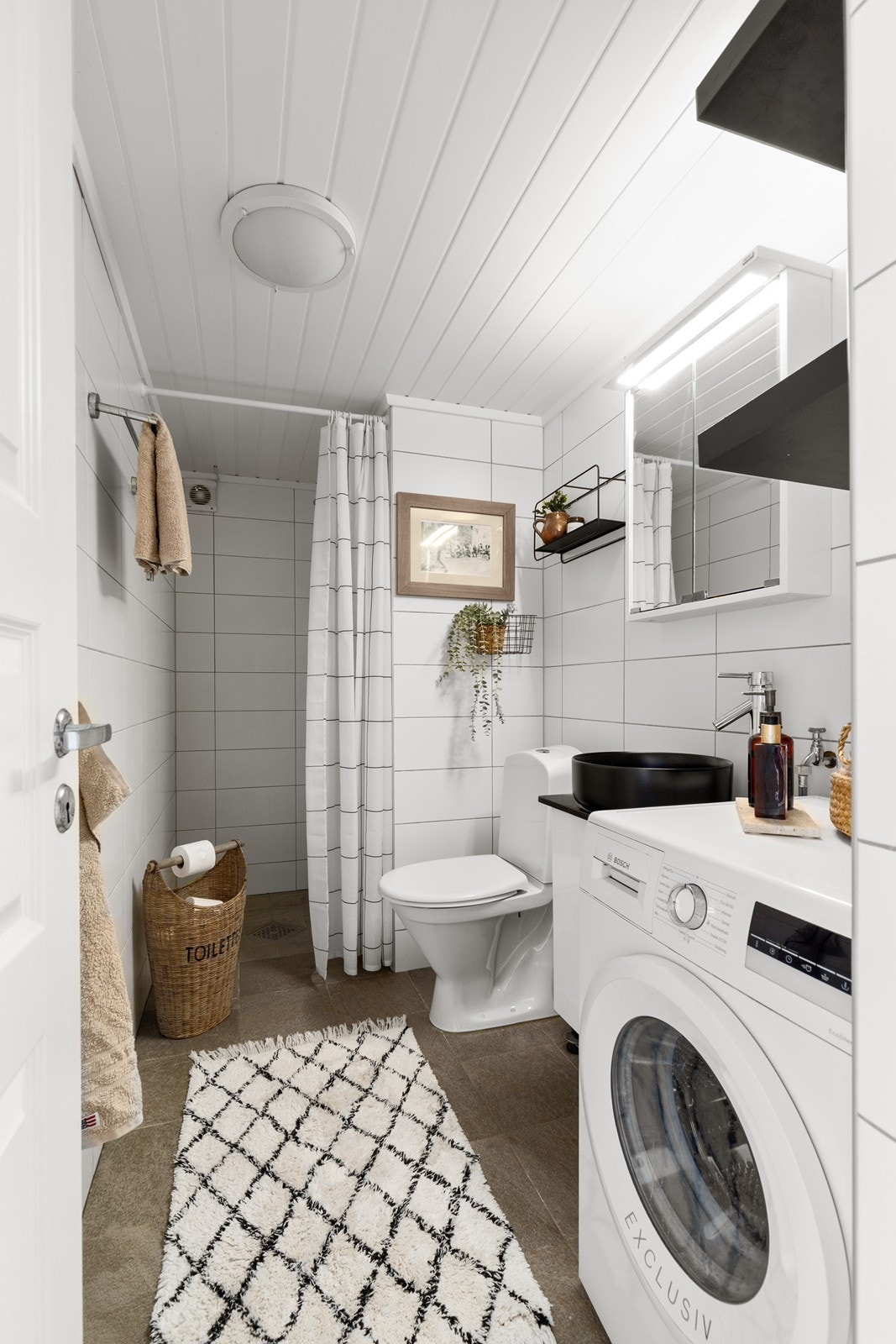 Klassisk og funksjonelt bad med baderomsinnredning bestående av servant med underskap, toalett og dusjnisje. Badet har også opplegg for vaskemaskin. Galleribilde