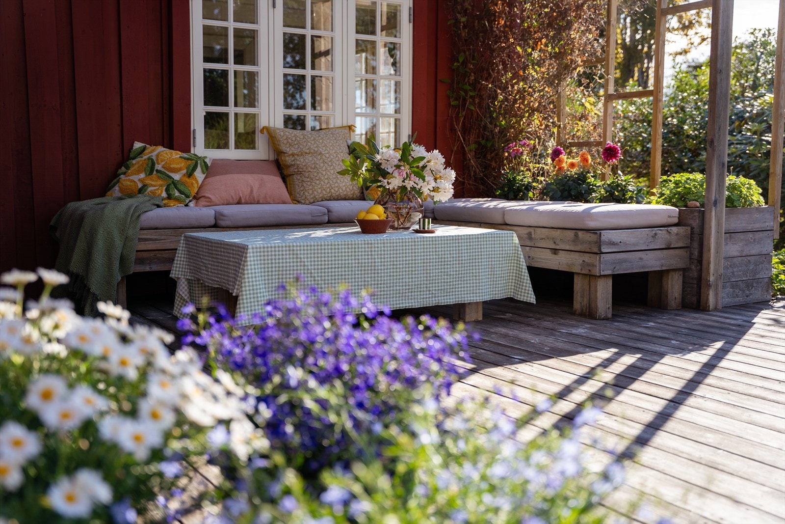 Hovedterrassen med plassbygde sittebenker og blomster i forgrunnen - direkte utgang fra kjøkken. Galleribilde