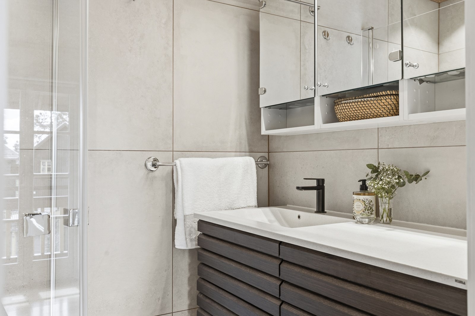 Badet er innredet med vegghengt toalett og en moderne baderomsinnredning og speilskap. Dusjnisje med mosaikkfliser og innfellbare glassdører Galleribilde