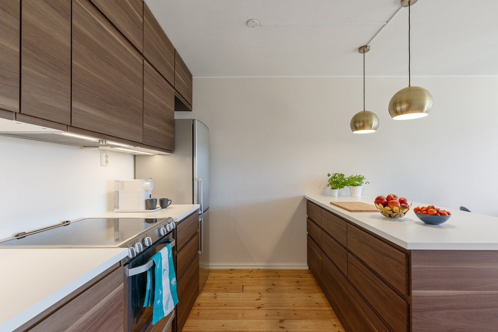 Kjøkkeninnredning fra IKEA med slette finerte fronter, laminat benkeplate, rustfri oppvaskkum, ventilator med kullfilter og frittstående hvitevarer som komfyr og kombinert kjøle- og fryseskap samt innebygget oppvaskmaskin. Galleribilde