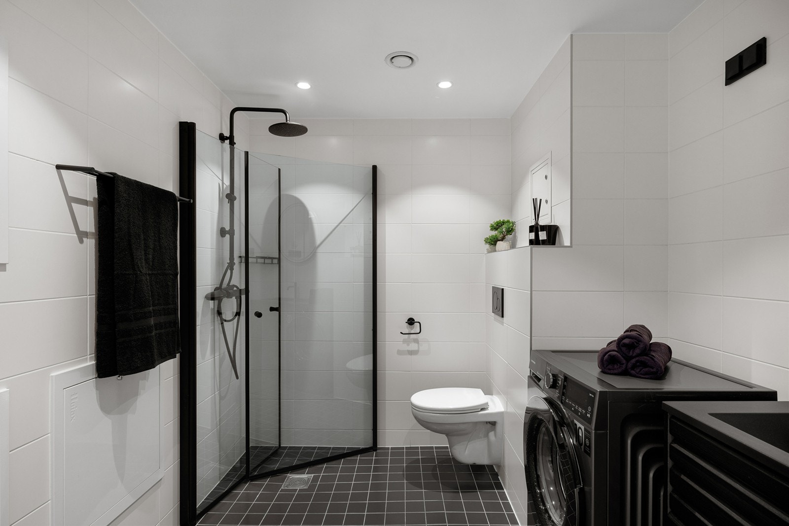 Delikat og moderne bad med flislagte gulv og vegger. Badet er innredet med servant med underskap, speil med belysning, dusjsone med glassvegger samt vegghengt toalett. Galleribilde