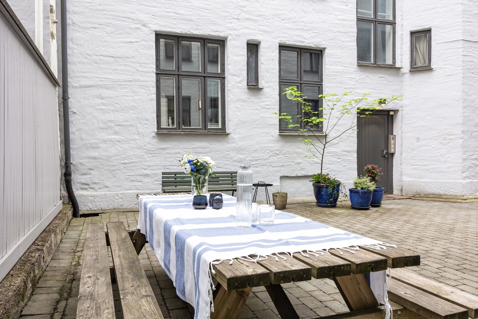 Bakgård belagt med belegningsstein og har beplantning, sittegruppe og sykkelparkering. Galleribilde