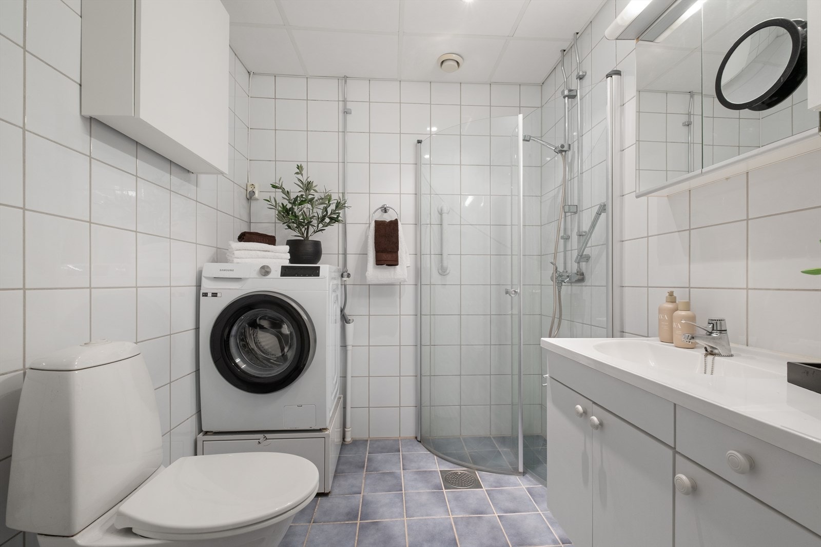 Tidløst bad som er utstyrt med dusjhjørne med buede svingbare skjermvegger, klosett, hel nedfelt servant, opplegg for vaskemaskin. Galleribilde