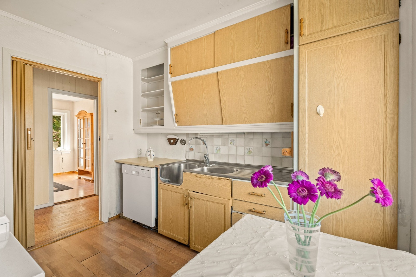 Dagens løsning gir godt med skapplass i to parallelle seksjoner, og innredningen har glatte fronter, åpne hyller, benkeplate av laminat og dobbel oppvaskkum i stål. Galleribilde