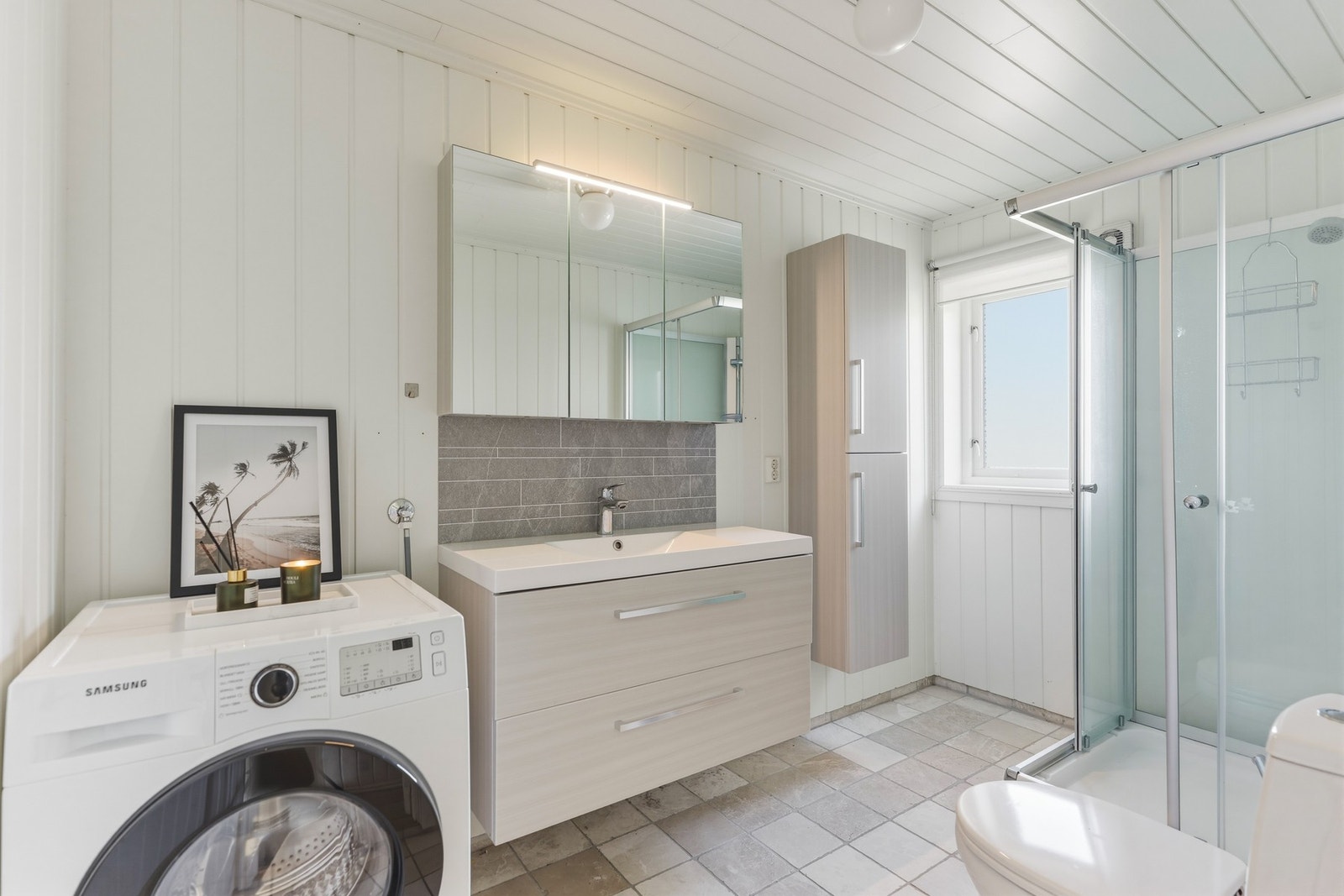 Baderom med flislagt gulv. Badet er av god størrelse og inneholder toalett, dusjkabinett og innredning med servant. og speilskap. Opplegg til vaskemaskin Galleribilde