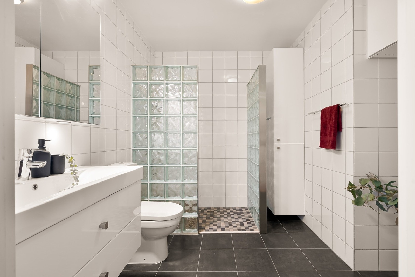 Det romslige badet er innredet med toalett, servant med skuffer under, vegghengt høyskap og stor dusjnisje. Galleribilde