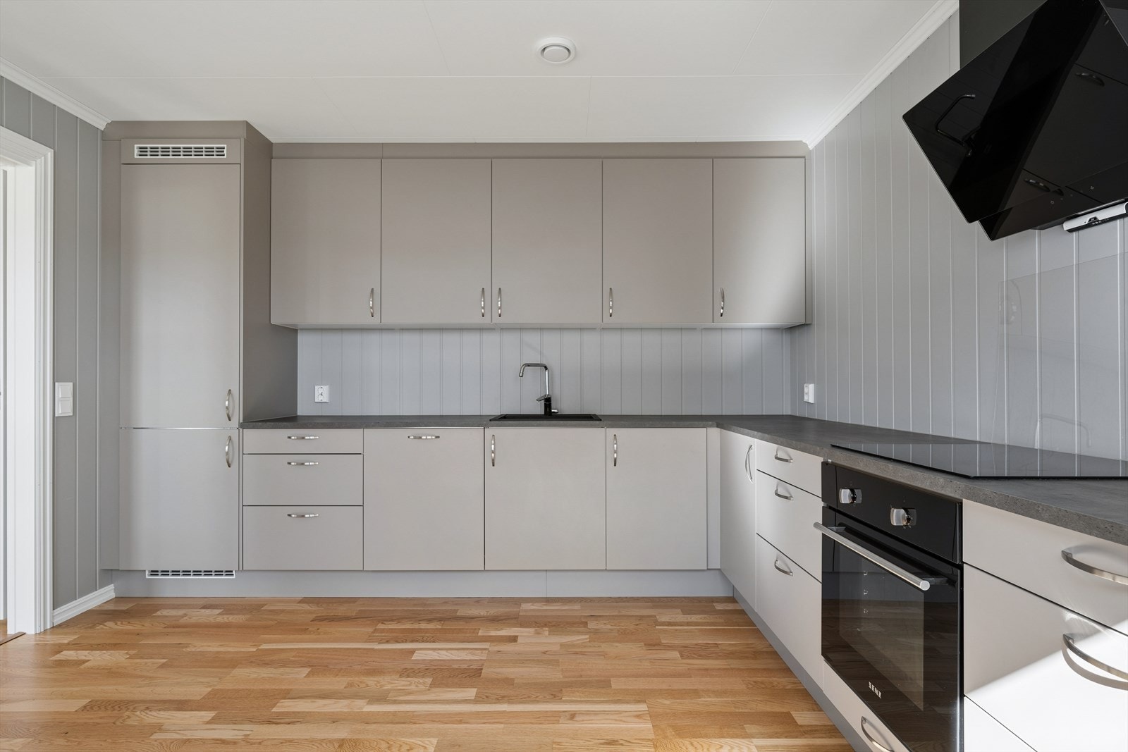 Kjøkkenet har en lekker og tidløs innredning fra Nybo med lyse, glatte fronter og mørk laminatbenkeplate med nedfelt kjøkkenkum. Galleribilde
