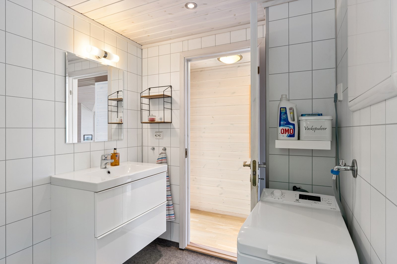 Badet har baderomsplater på veggene, vinylbelegg på gulv og opplegg for vaskemaskin. Galleribilde