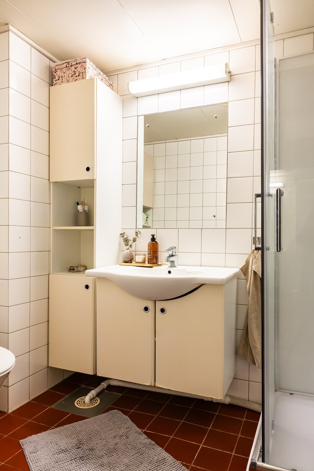 Flislagt baderom fra byggeår med varmekabler i gulv. Badet er innredet med gulvstående toalett, dusjkabinett og servant med skapinnredning. Galleribilde