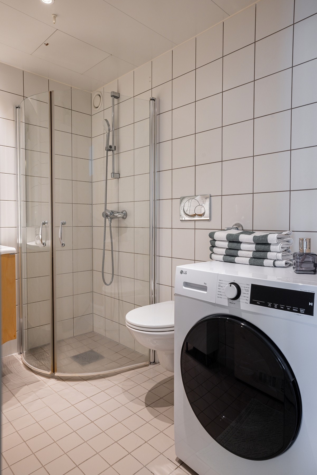 Baderommet er også utstyrt med dusjhjørne med innfellbare glassdører og veggmontert hånddusj samt vegghengt toalett. Termostatstyrte varmekabler i gulv. Nedsenket himling med downlights. Galleribilde