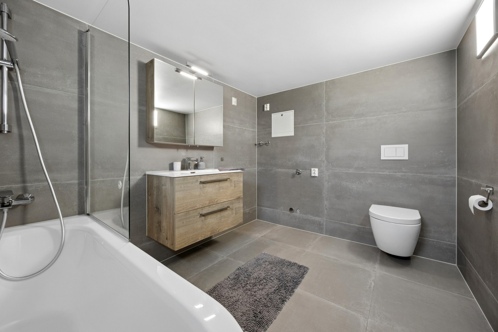 Badet er utstyrt med badekar med dusjløsning, vegghengt toalett og servantinnredning med speilskap. Galleribilde