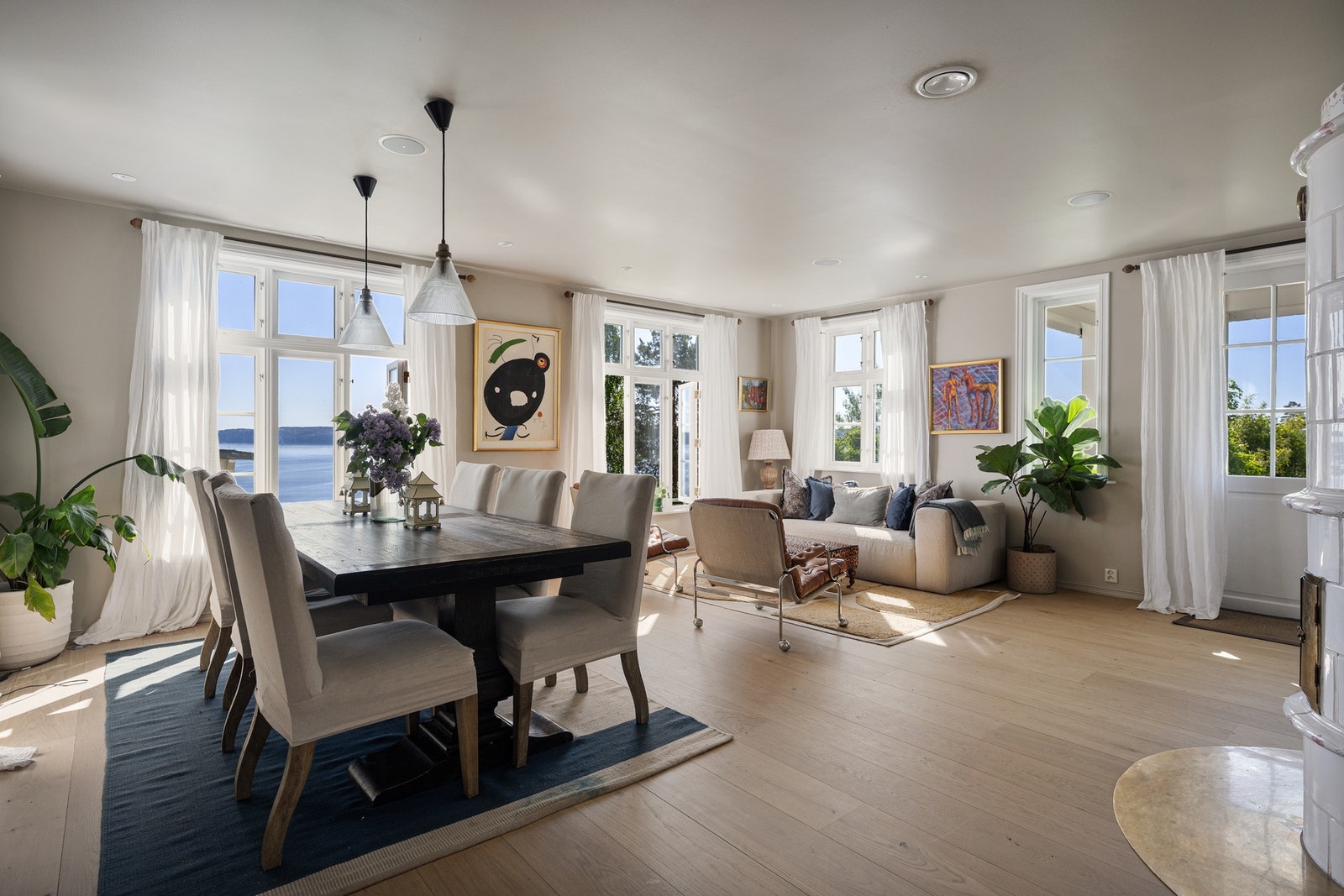 Lys og innbydende stue med store vindusflater som rammer inn den vakre fjordutsikten. Den åpne løsningen mellom stue og spisestue skaper en luftig og sosial atmosfære med rikelig lysinnslipp. Galleribilde
