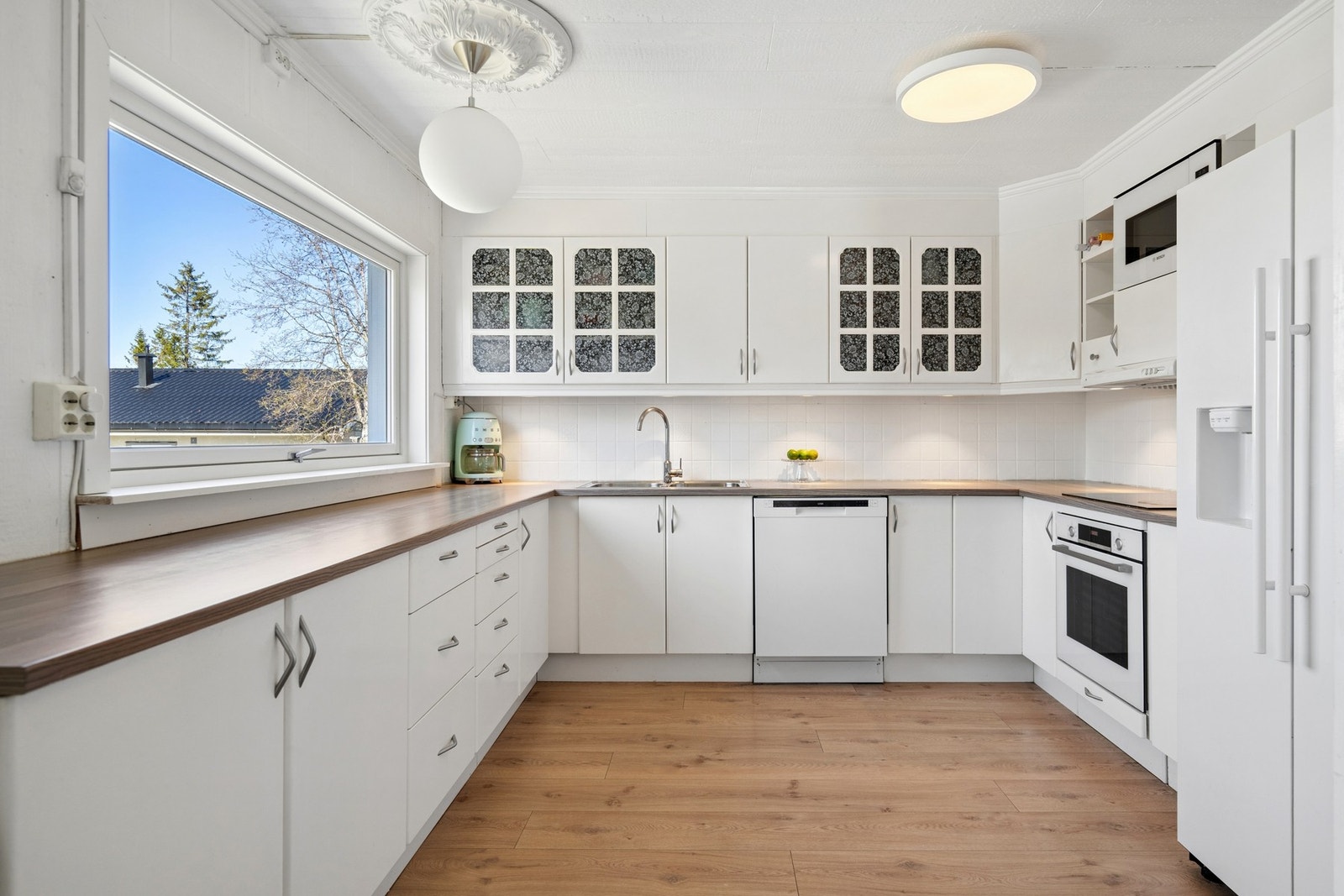Kjøkkeninnredning med laminerte fronter og benkeplate. Det er belysning under overskapene og fliser på veggen over benken. Galleribilde