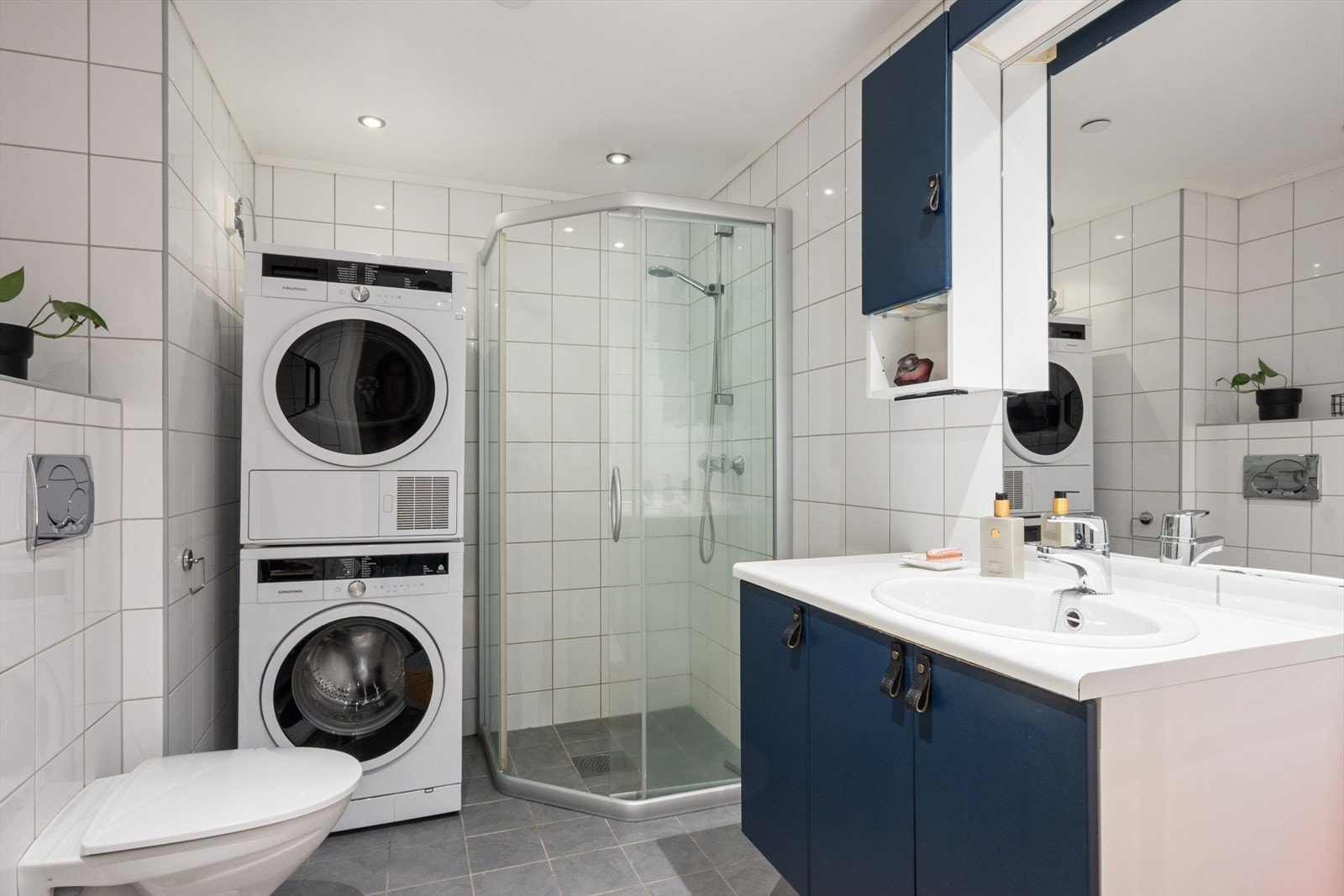 Badet er innredet med baderomsinnredning med benkeplate og nedfelt servant, vegghengt toalett og dusjhjørne med dører i herdet glass. Det er opplegg for vaskemaskin. Galleribilde