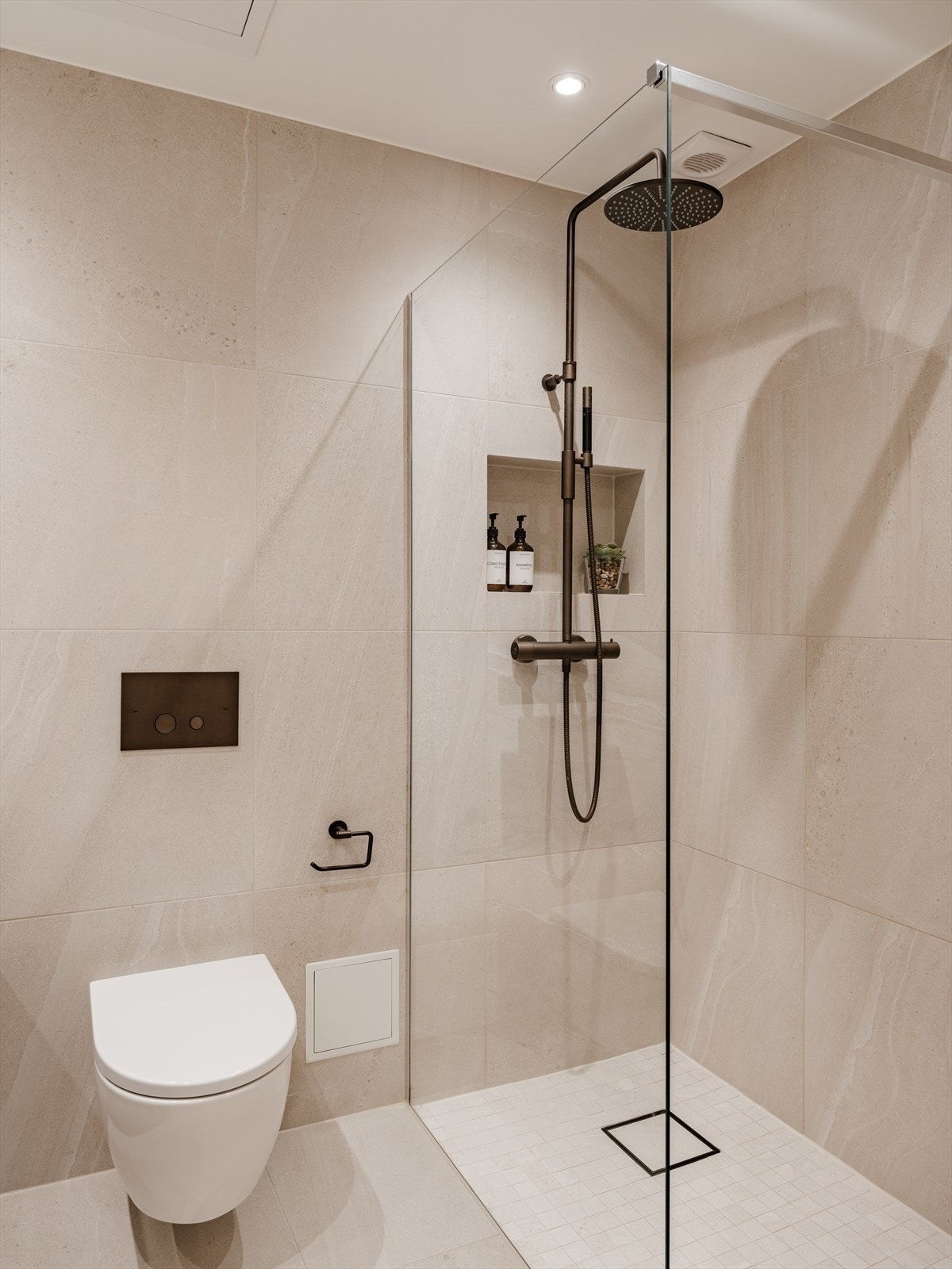 Badet er utstyrt med gulvvarme og mekanisk avtrekk. Videre finner du vegghengt WC, romslig dusjplass med fastmontert glassvegg samt integrert hylle, og servant med ettgreps blandebatteri i moderne innredning. Galleribilde