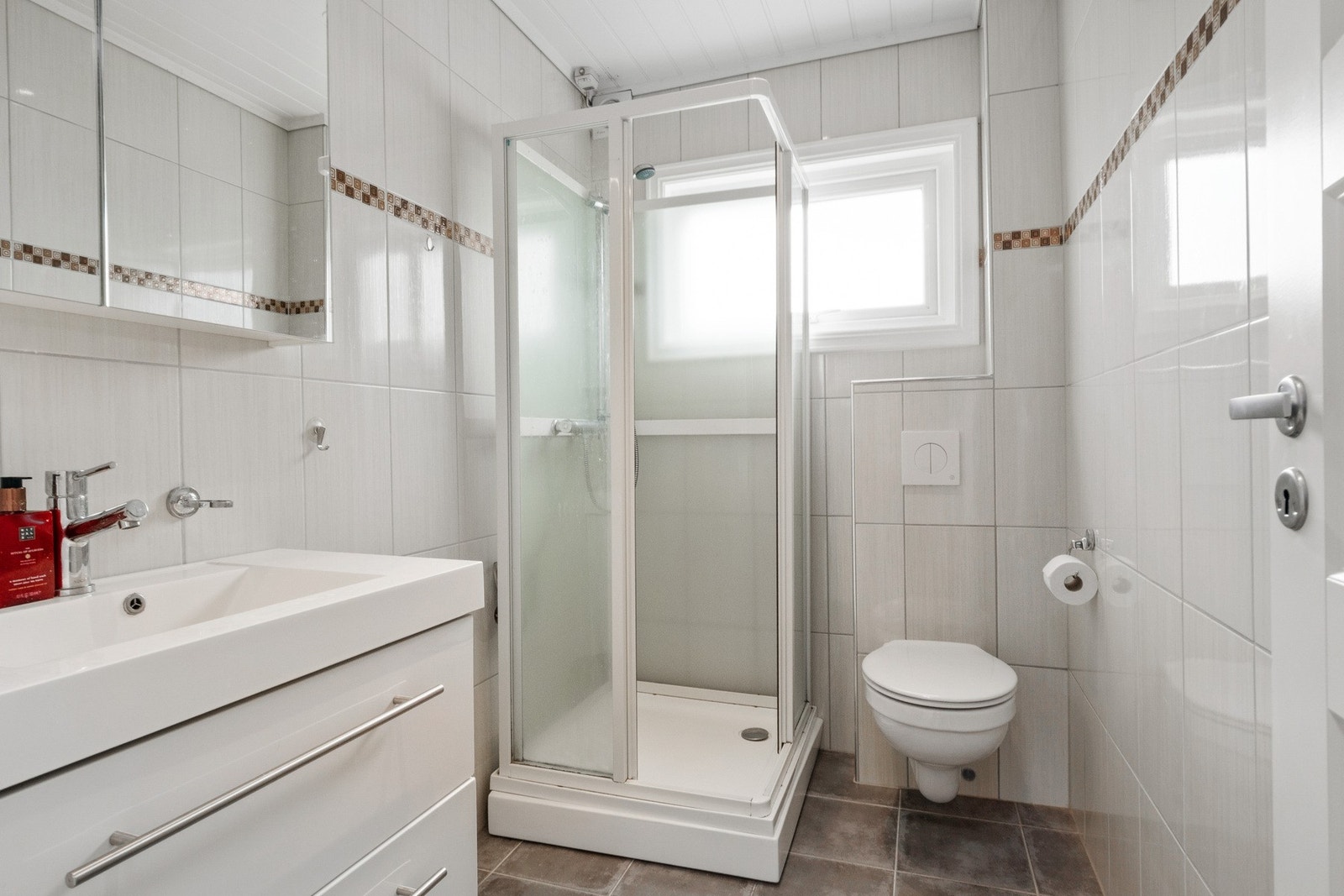 Badet er fra 2014 og har fliser på vegg og gulvvarme under flisene. Her finner du praktisk innredning med servant, dusjkabinett og veggmontert toalett. Galleribilde