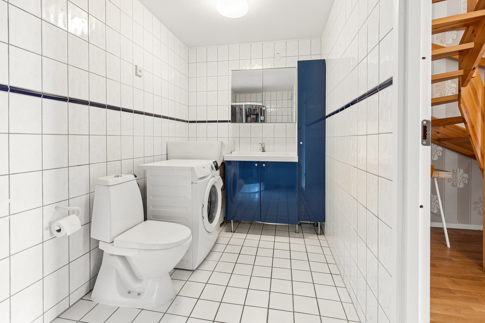 Flislagt bad med servantinnredning, gulvstående toalett, dusjkabinett og opplegg for vaskemaskin. Galleribilde