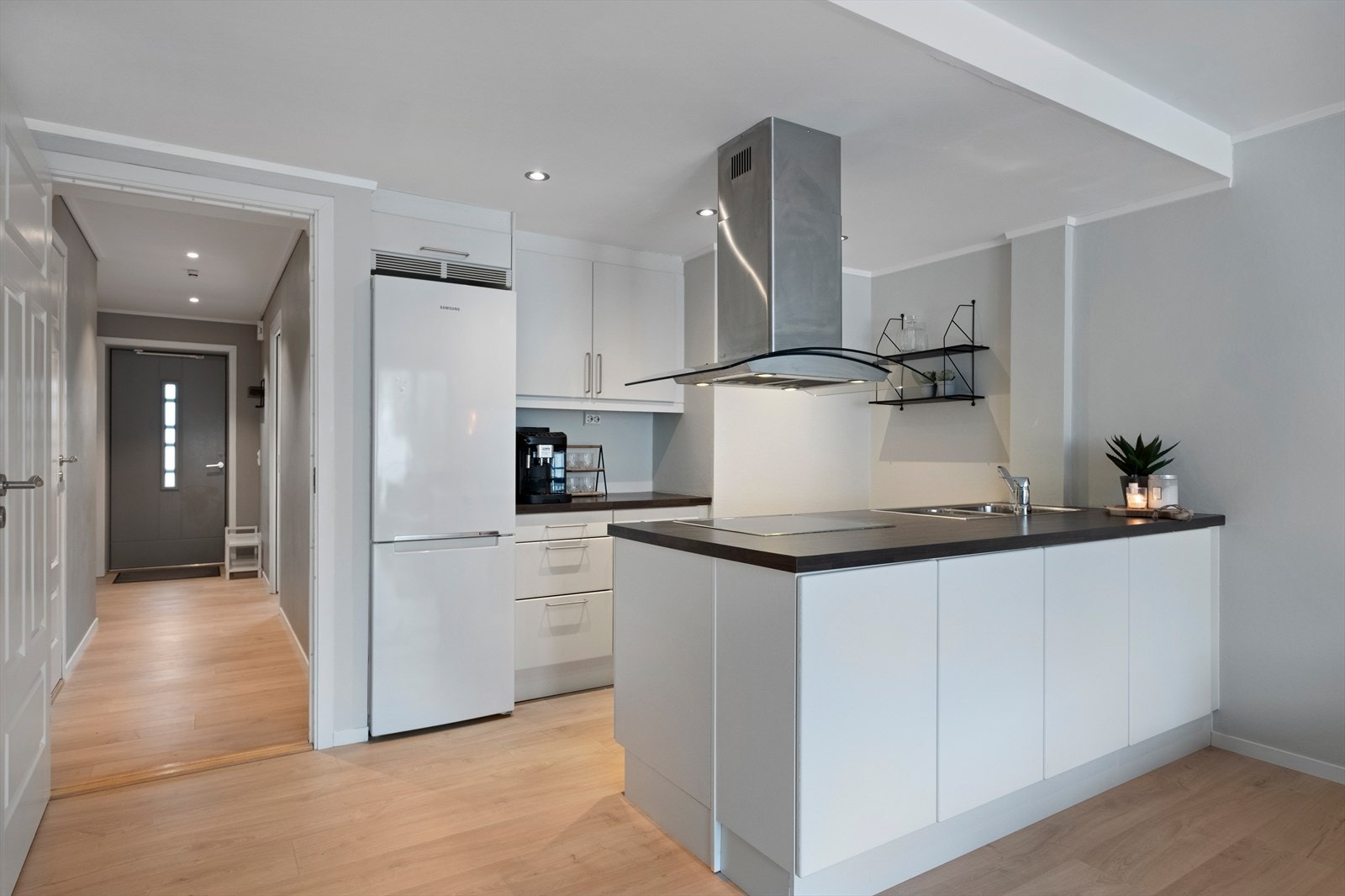 Kjøkkeninnredning fra Sigdal med hvite fronter i laminatutførelse og stålhåndtak. Laminatbenkeplate med oppvaskkum i rustfritt stål. Integrert platetopp, stekeovn og oppvaskmaskin. Nisje for kjøleskap. Galleribilde