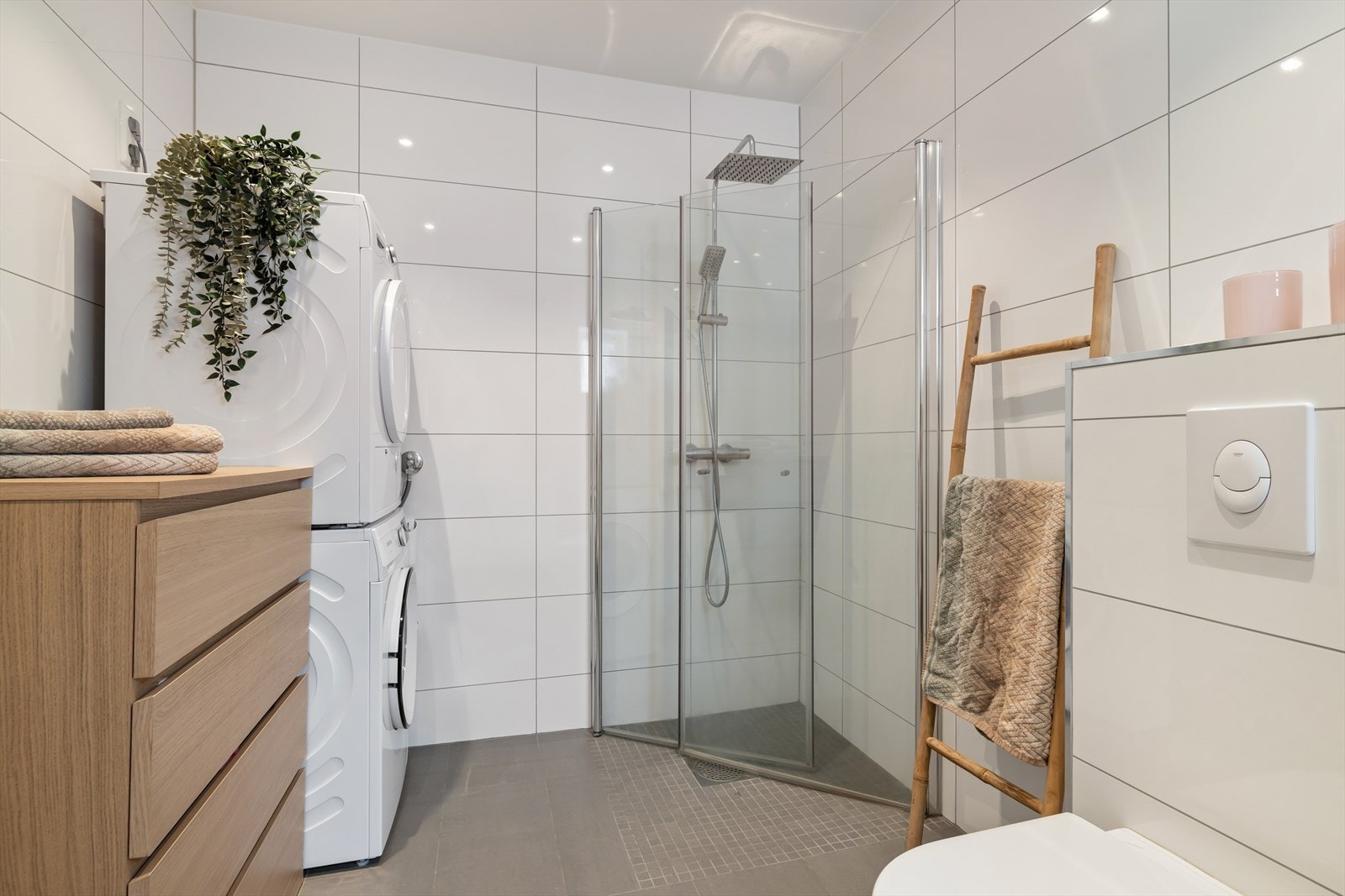 Badet er kombinert vaskerom med opplegg for vaskemaskin og har en praktisk dusjnisje med innfellbare dører. Galleribilde