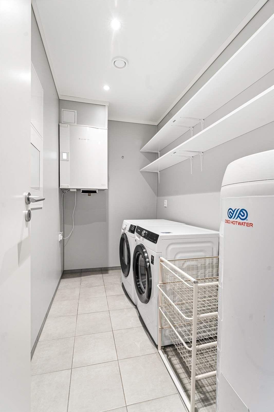 Praktisk vaskerom med flislagt gulv, opplegg for vaskemaskin og boligens tekniske installasjoner. Galleribilde