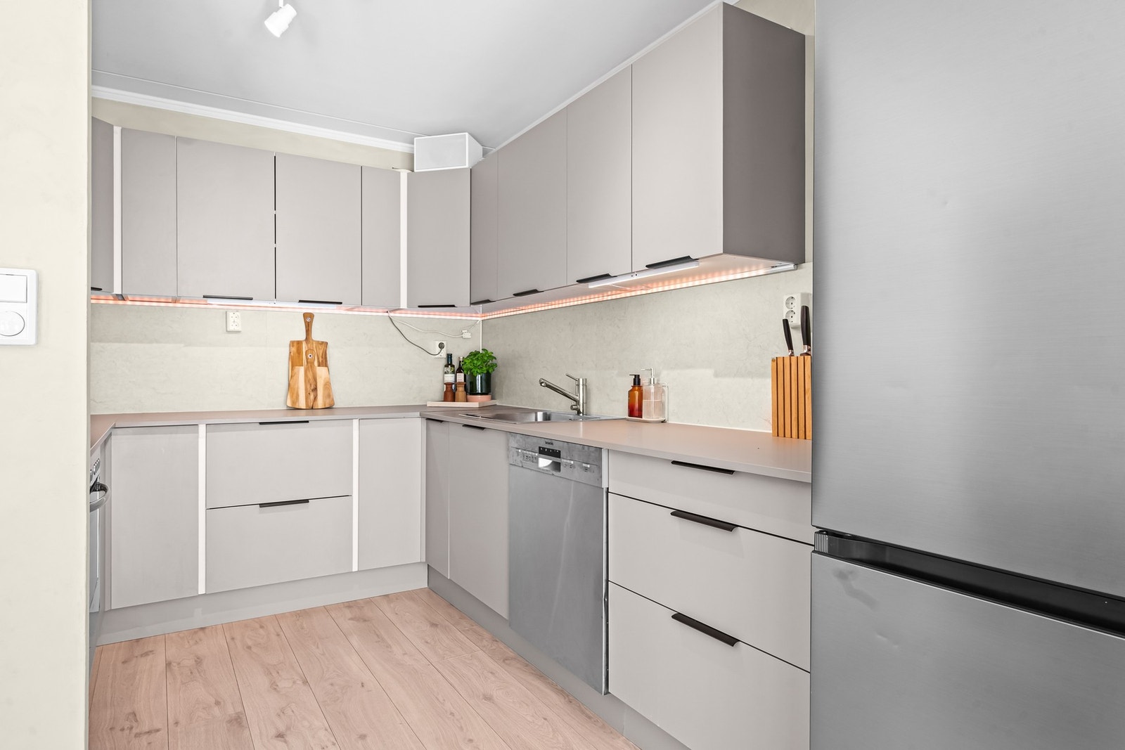 Moderne og velholdt kjøkken med stilrene fronter i en lun gråbeige tone, integrert oppvaskmaskin, platetopp og stekeovn - oppdatert med nye fronter og benkeplate. Galleribilde