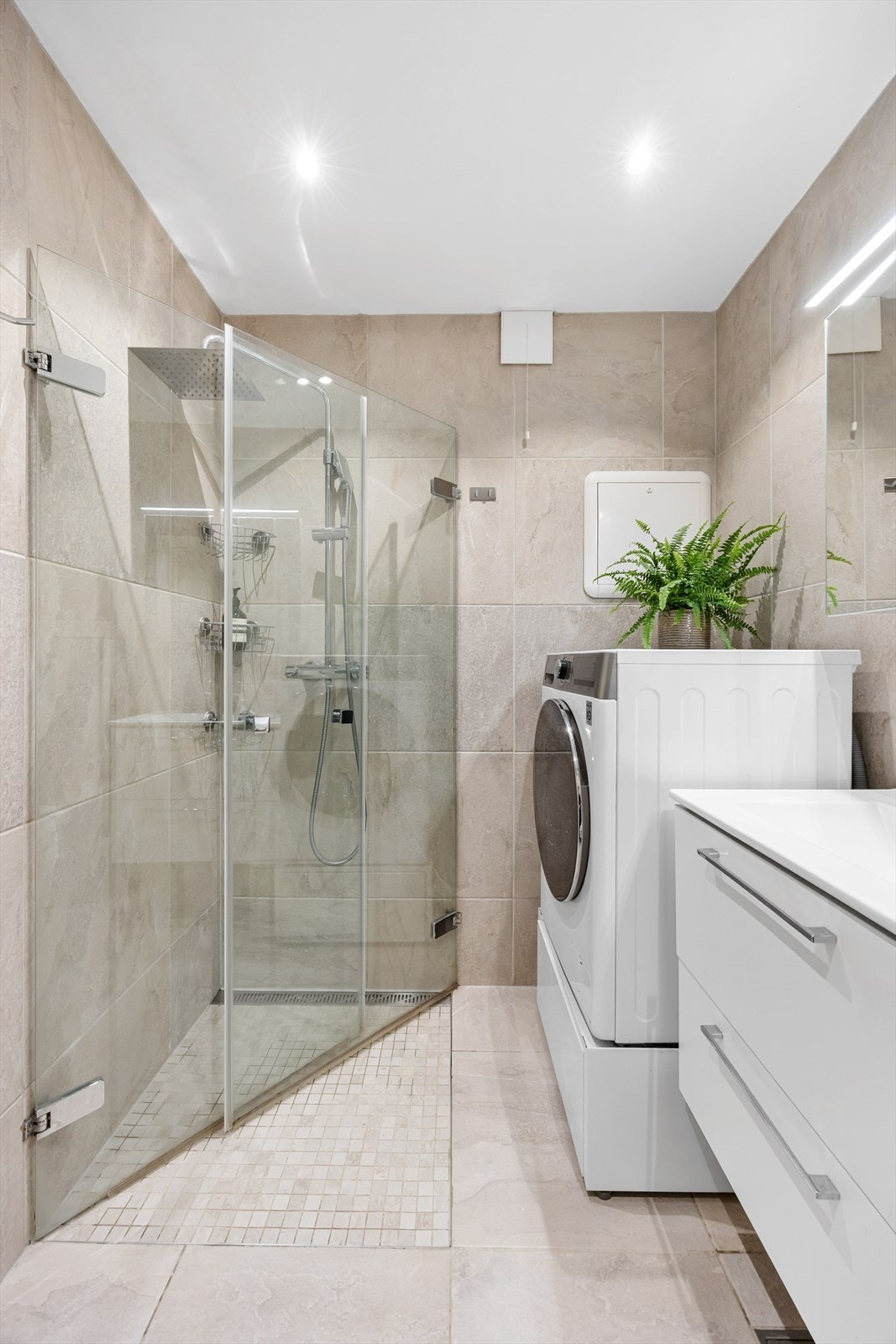 Badet er utstyrt med innredning med servant og glatte fronter, vegghengt toalett, dusj på gulv og opplegg for vaskemaskin. Galleribilde