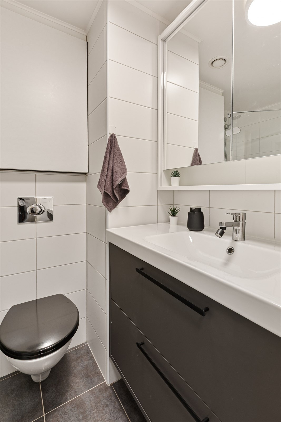 Badet er utstyrt med vegghengt toalett, dusjhjørne med glassdør, innredning med servant, speilskap, samt veggskap. Galleribilde