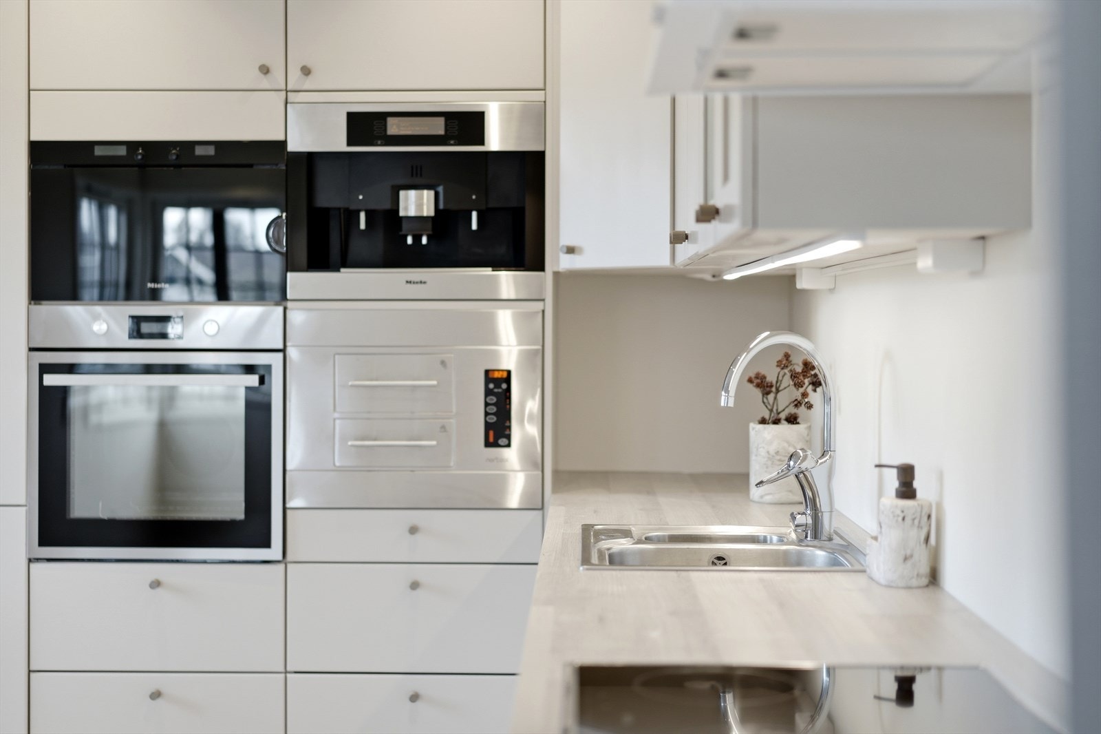 Lekre detaljer, herunder bl.a. med kaffemaskin fra Miele. Hvitevarene er plassert i komfortabel høyde i høyskapet. Galleribilde