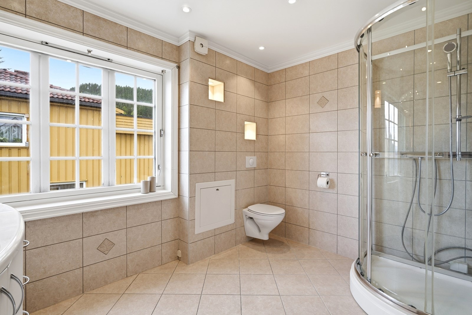 Flislagt med dusjkabinett, rør-i-rør, dusjkabinett og downlights i himling. Det er egne veggnisjer med integrert belysning over toalettet. Galleribilde