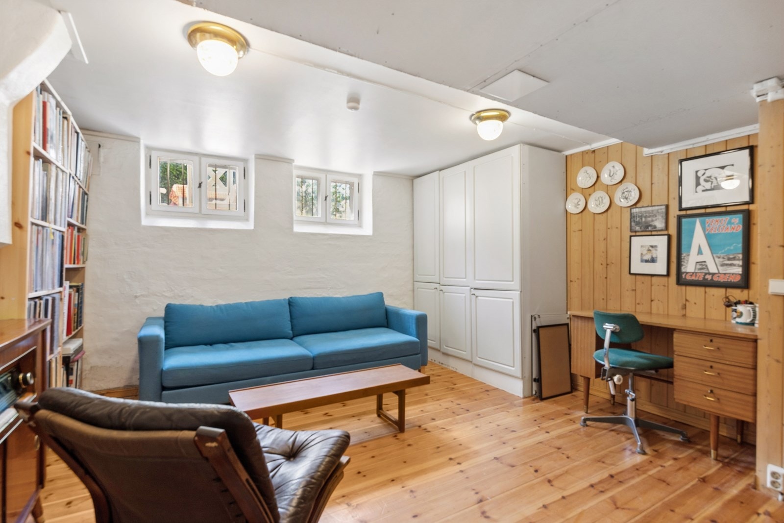 Kjellerom som er innredet med gulv, sofa, skrivebord og garderobeskap. Her er det potensiale for videre utvikling. Per i dag er kjelleren fellesareal som leiligheten disponerer. Galleribilde