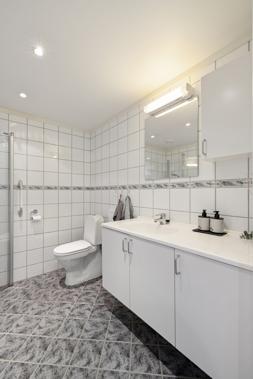 Badet er innredet med servant med underskap, speil med tilhørende belysning, dusjdører og gulvmontert toalett. Det er også opplegg for vaskemaskin. Galleribilde