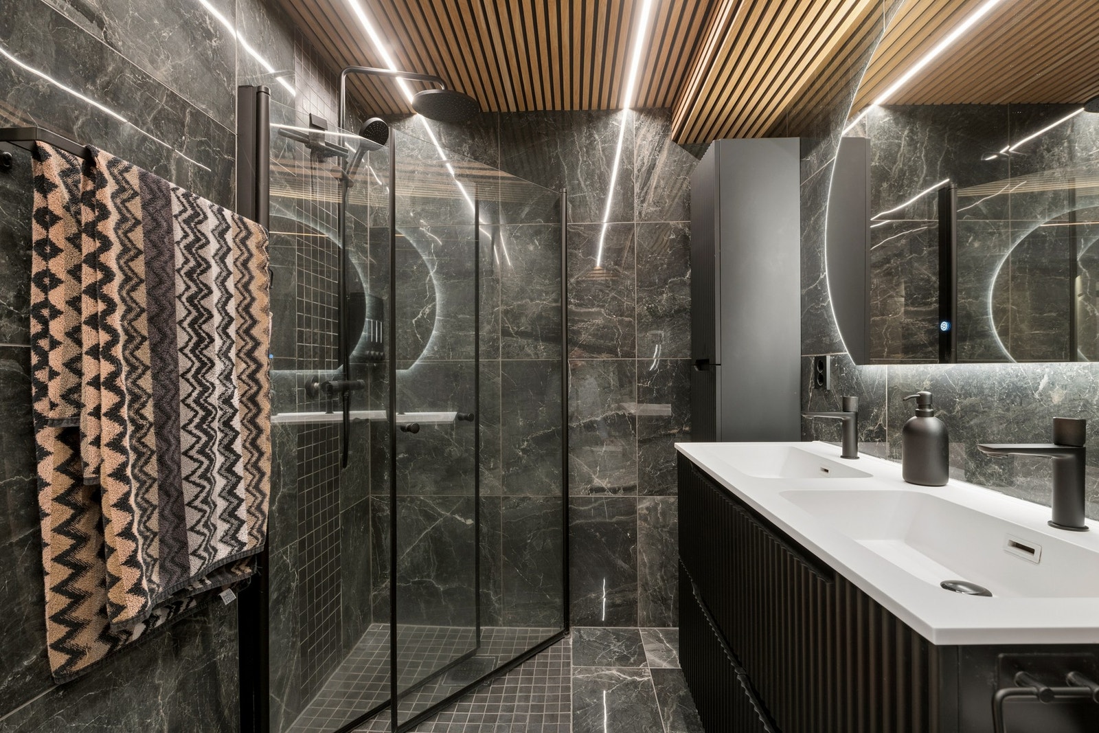 Badet har romslig dusjhjørne med glassdører og sort armatur - gjennomført i samme høye standard som resten av rommet. Galleribilde