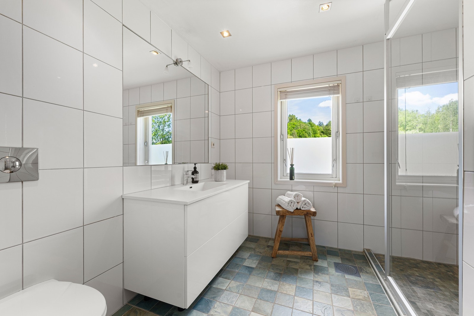 Badet i 2. etasje er flislagt og innredet med servantskap, heldekkende servant, speil med lysarmatur, dusjhjørne og veggmontert toalett. Galleribilde