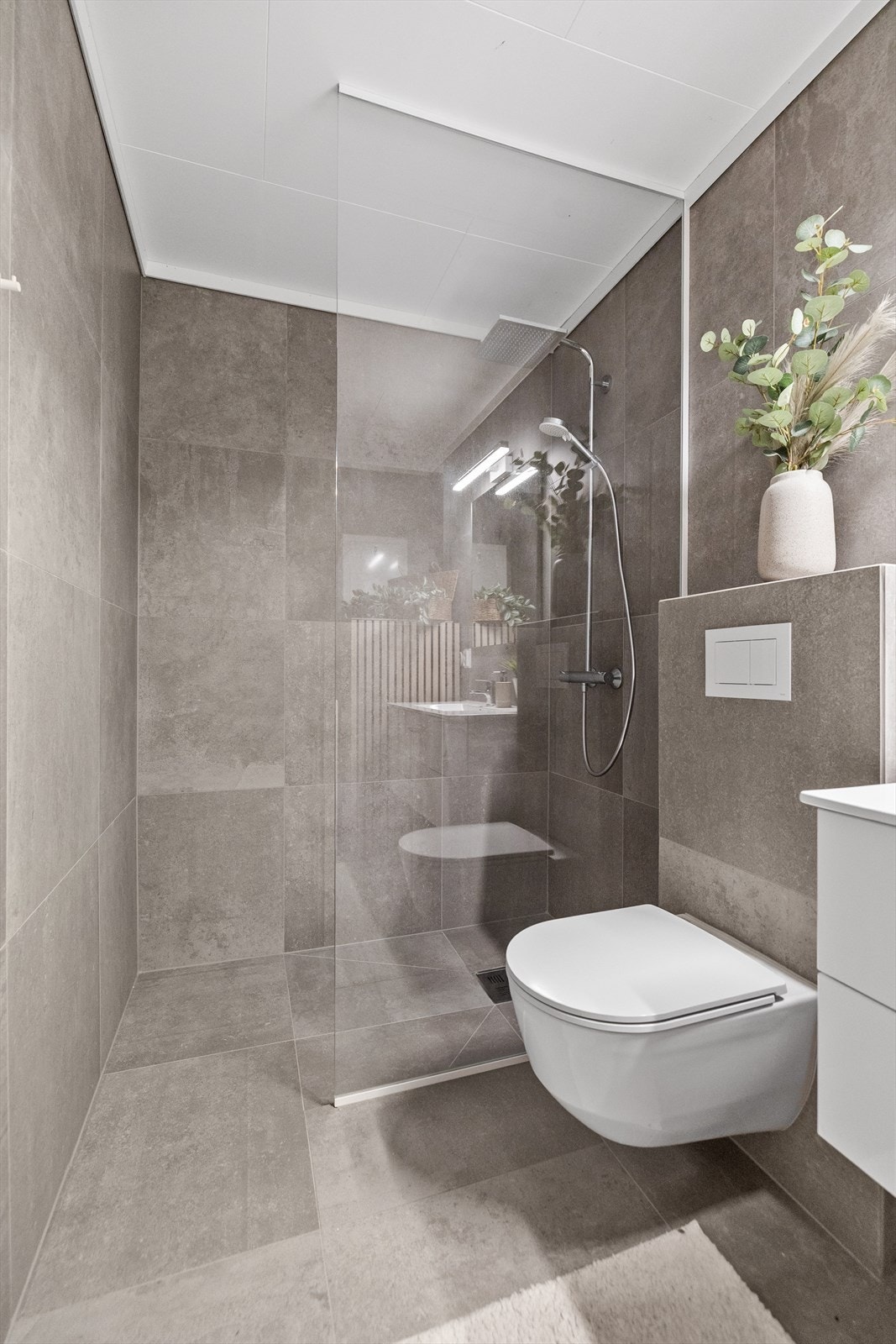Badet er innredet med vegghengt toalett, servant med innredning, speil og dusjnisje med glassvegg som gir et eksklusivt og helhetlig uttrykk. Galleribilde