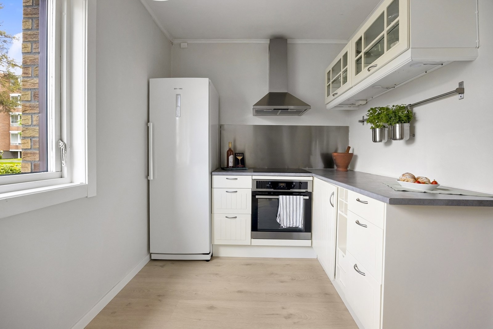 Et tidløst og innbydende kjøkken med profilerte fronter og enkelte overskap med glassfronter. Integrert belysning under overskapene og stålplate over benkeskapene gir både et praktisk og stilrent uttrykk. Laminat benkeplate. Galleribilde