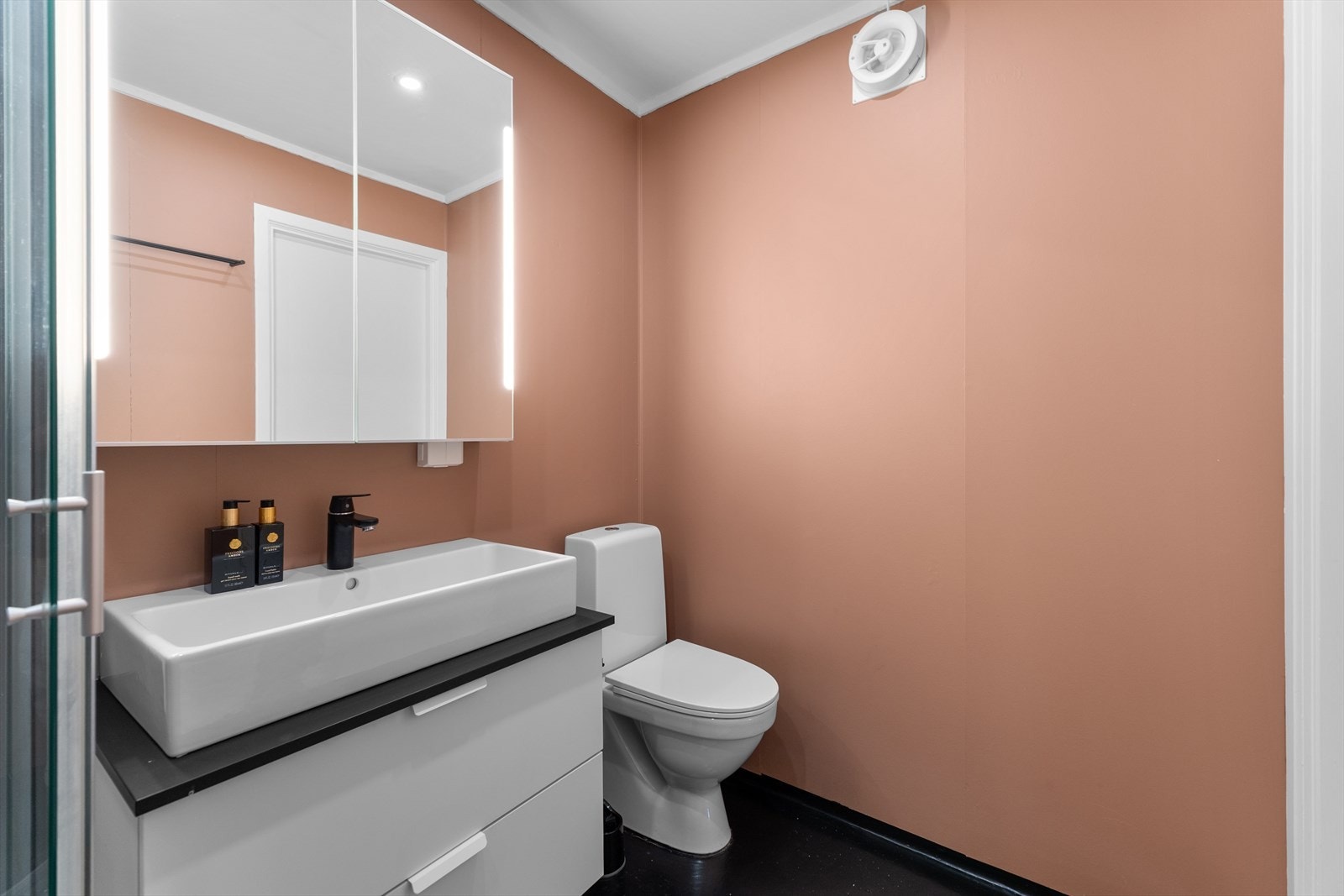 Badet holder en enkel, men fin standard med malte våtromsplater, malt vinyl, wc, dusjkabinett og servantskap. Galleribilde