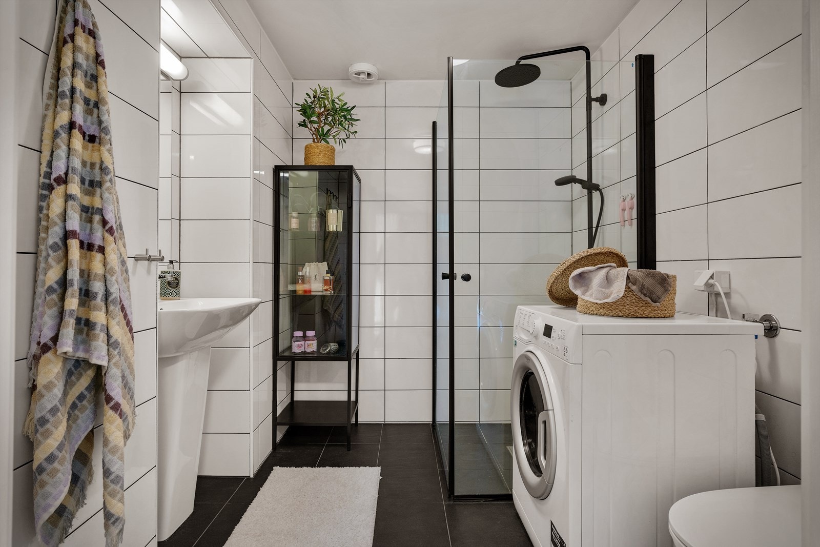 Badet er utstyrt med servant, veggmontert toalett, dusjløsning og opplegg for vaskemaskin. Dusjvegger og garnityr er fra 2024, og toalett er nytt i 2026. Galleribilde