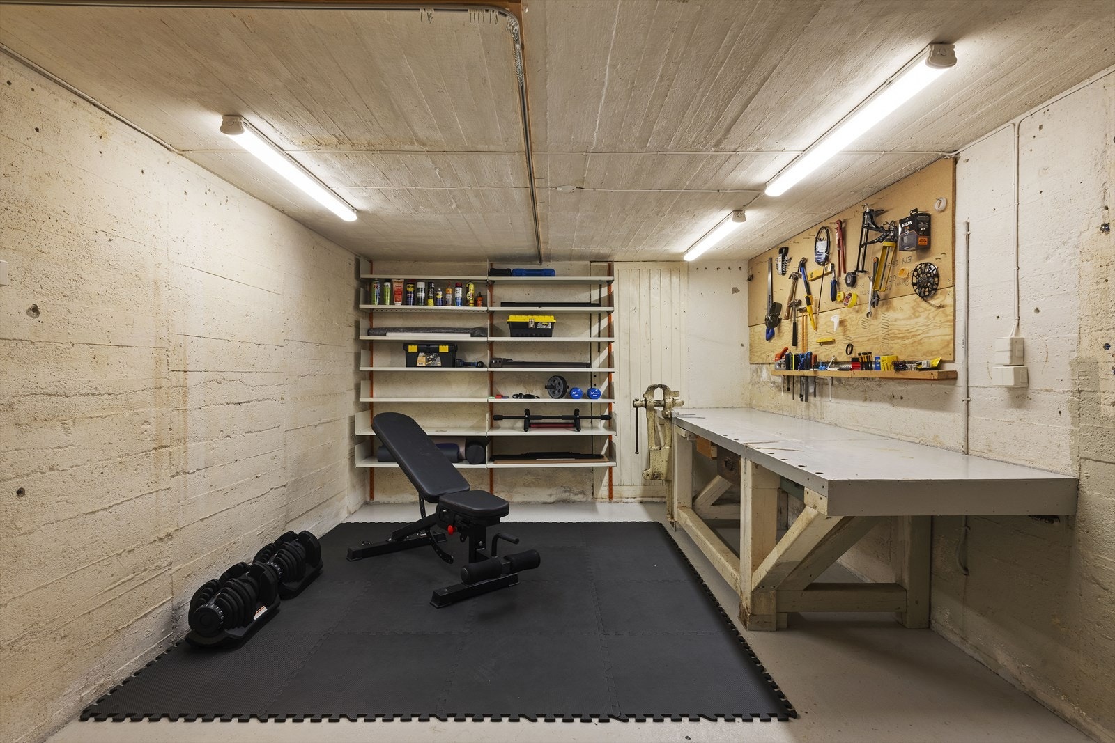 Kjelleren byr også på et stort, støpt rom som i dag er innredet som et kombinert treningsrom og verksted/hobbyrom. Dette er det perfekte stedet for deg som ønsker plass til styrketrening, snekring, sying eller andre plasskrevende hobbyer. Galleribilde