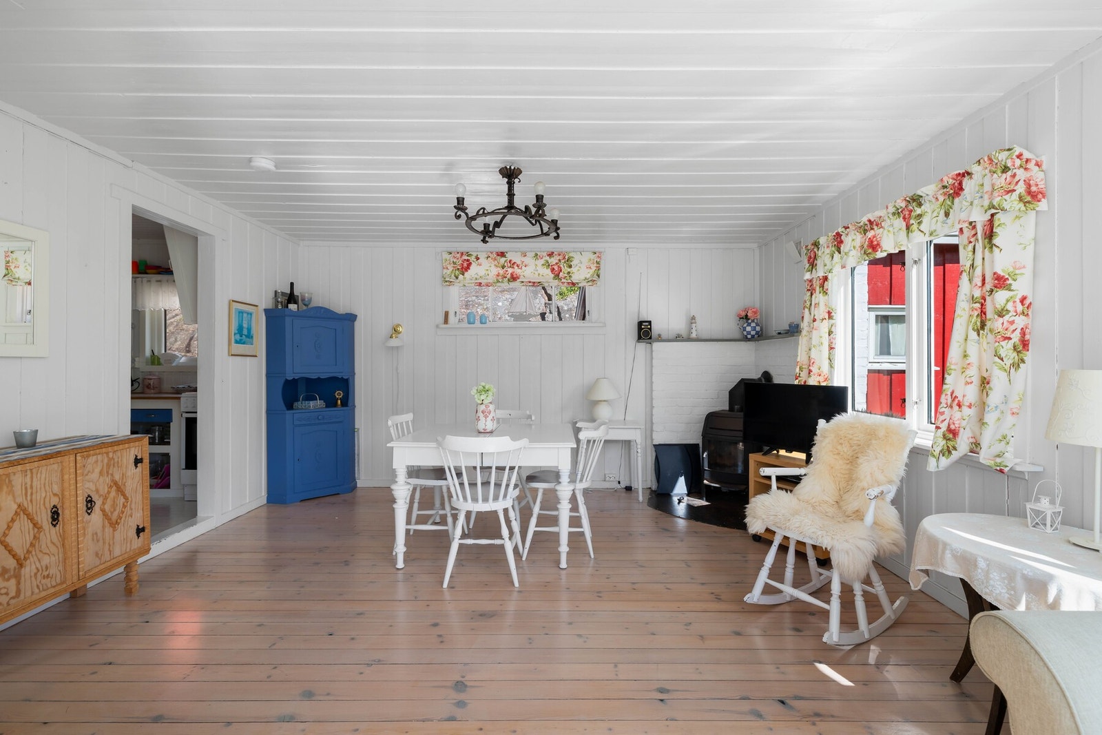 Rommet har lyst tregulv, hvitmalte panelvegger og hvitmalt panelhimling. I hjørnet av stuen er det satt inn en vedovn som varmer godt. Galleribilde