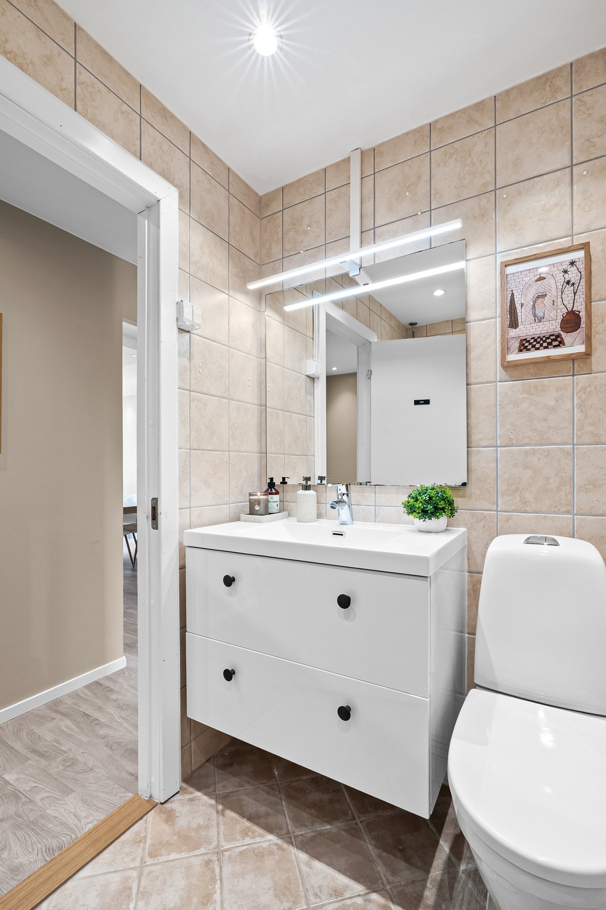 Badet er utstyrt med heldekkende servant, speil med lysarmatur, gulvmontert klosett og dusjhjørne med svingdører. Galleribilde