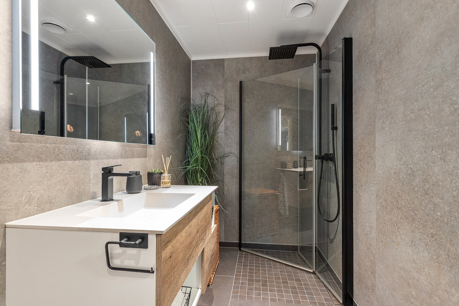 Badet er innredet med vegghengt klosett, servant med innredning, speil med lys og dusjhjørne med svingbare glassdører. Det er både plass og opplegg for vaskemaskin og tørketrommel. Dusjhjørnet har innfellbare glassdører og en regnfallsdusj. Galleribilde