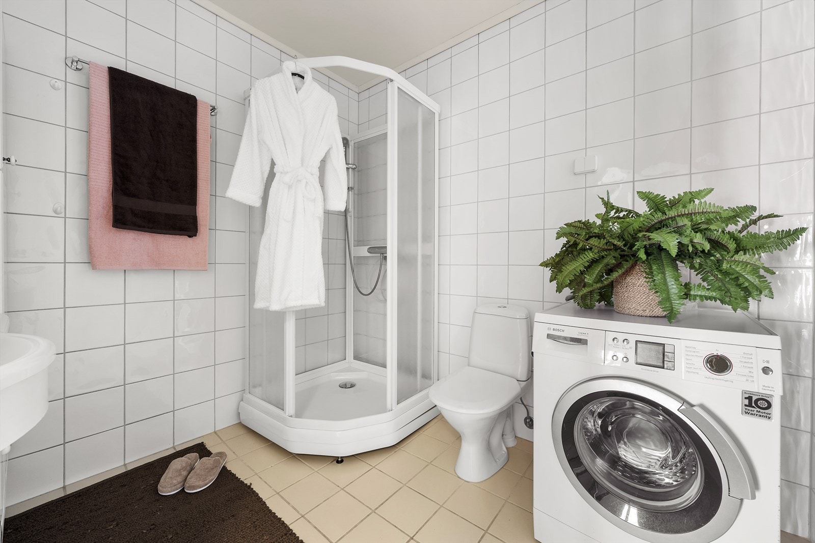 Badet er utstyrt med servant over skapinnredning, sideskap, toalett, dusjkabinett og opplegg til vaskemaskin Galleribilde