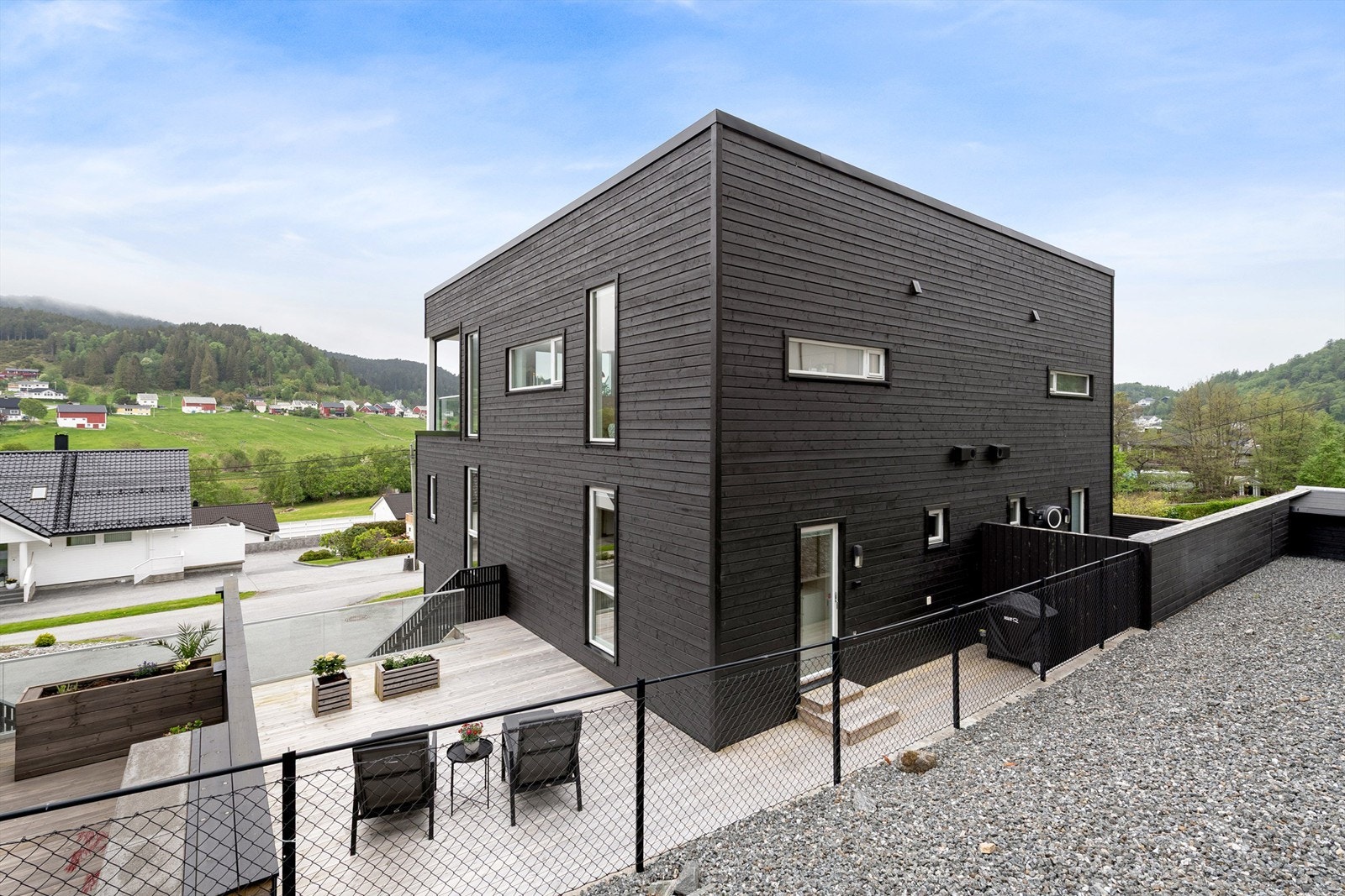 Fasade og terrasse mot nordøst. Stor terrasse på terreng med levegg mot naboer samt trapp til gårdsplass Galleribilde