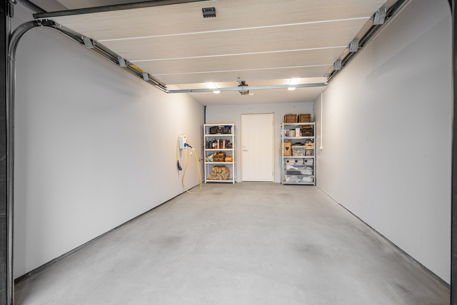 Integrert garasje med elbillader. Bak garasjen ligger to boder med tekniske installasjoner som sentralstøvsuger og ventilasjonsaggregat. Galleribilde