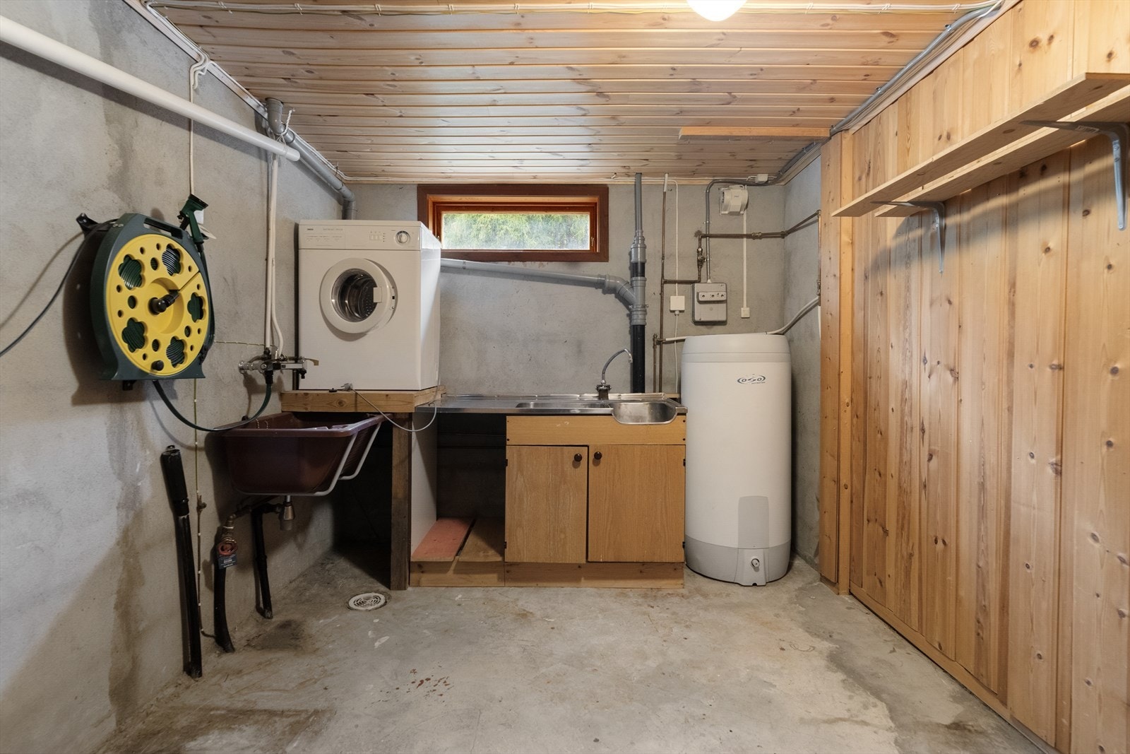 Praktisk vaskerom med betonggulv og opplegg for vaskemaskin. Her er også varmtvannsberederen fra 2016 og sentralstøvsugeren plassert. Galleribilde