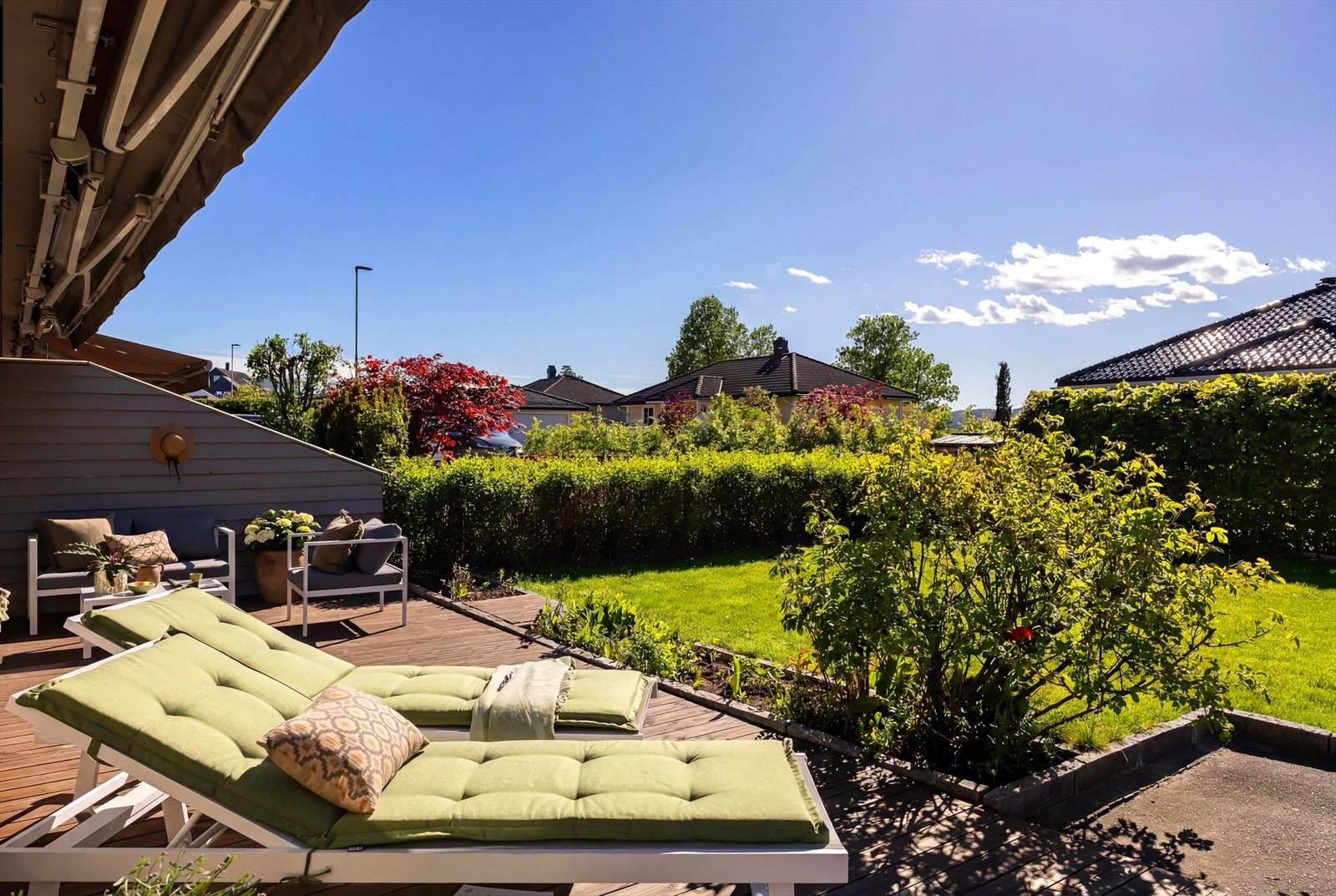 Uteplassen foran huset har en romslig terrasse med elektrisk markise og en frodig, grønn hage. Galleribilde