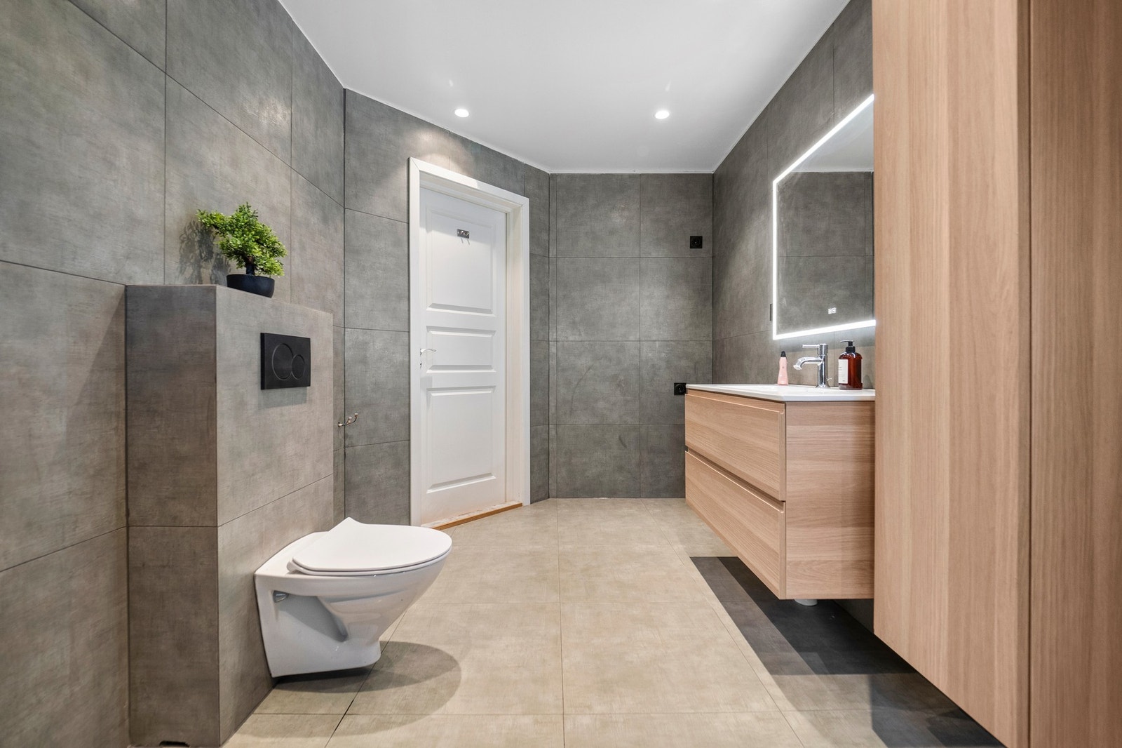 Badet har grå fliser på veggene, downlights i himlingen og lyse fliser på gulv med gulvvarme. Galleribilde