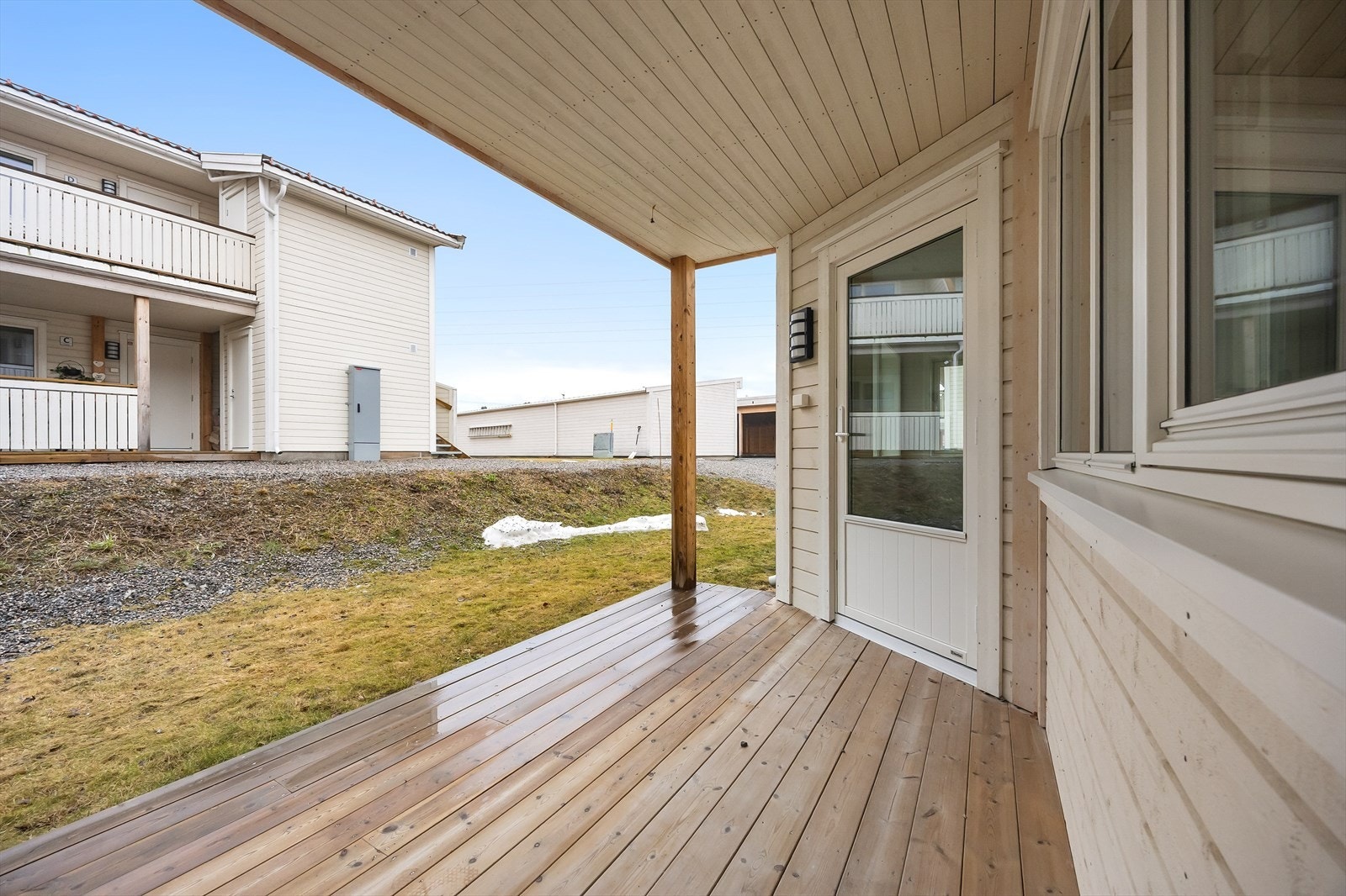 Fra uteplassen ser man mot fellesarealene og carportanlegget. Galleribilde