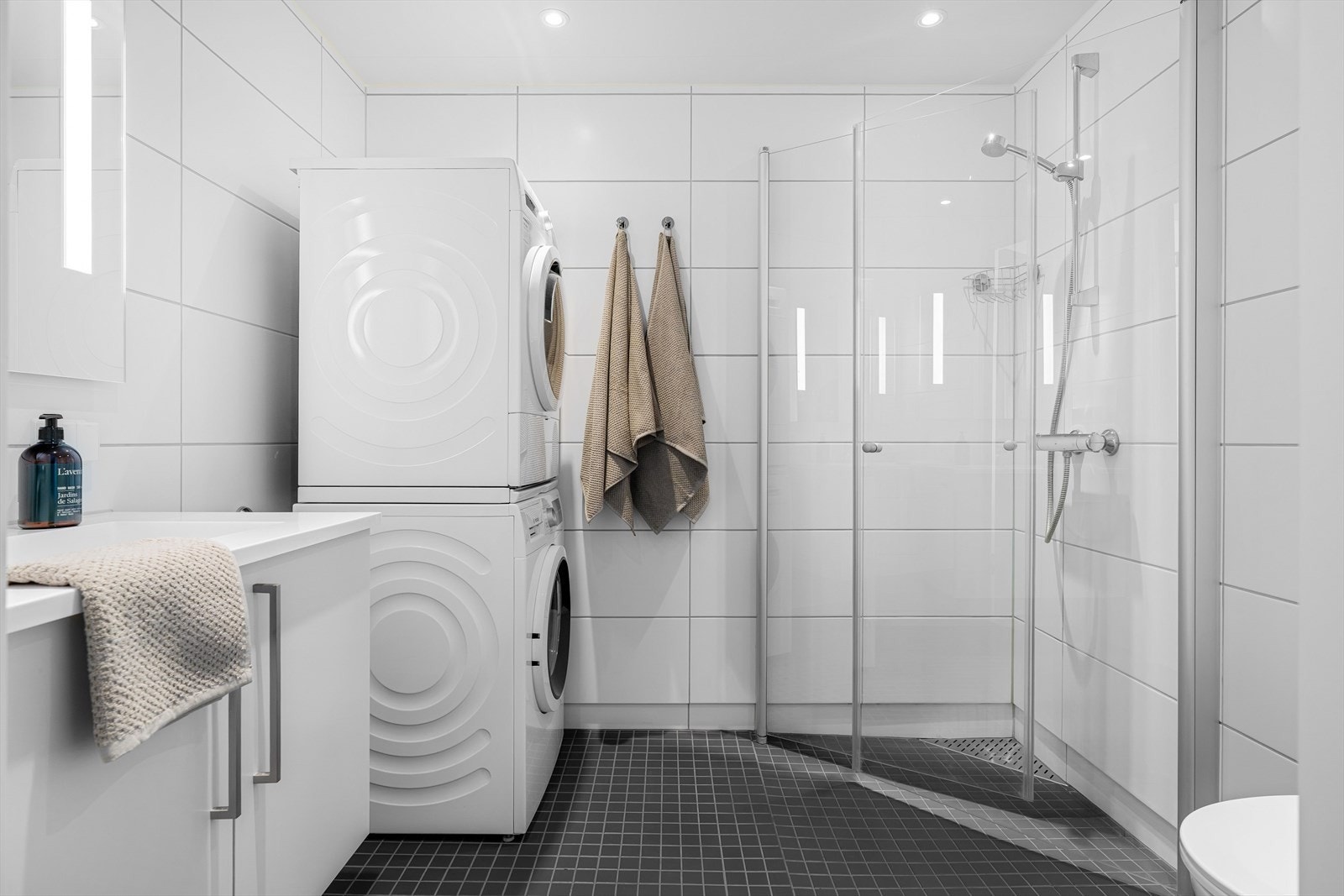 Badet er utstyrt med innredning fra HTH, speil med integrert belysning, opplegg for vaskemaskin, dusjhjørne med innfellbare dører, toalett og varmekabler i gulv. Galleribilde