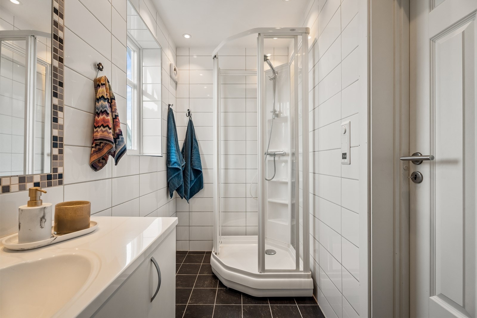 Badet fremstår som lyst, moderne og funksjonelt med hvite veggfliser og mørke gulvfliser i fin kontrast. Gulvet har behagelige elektriske varmekabler. Galleribilde